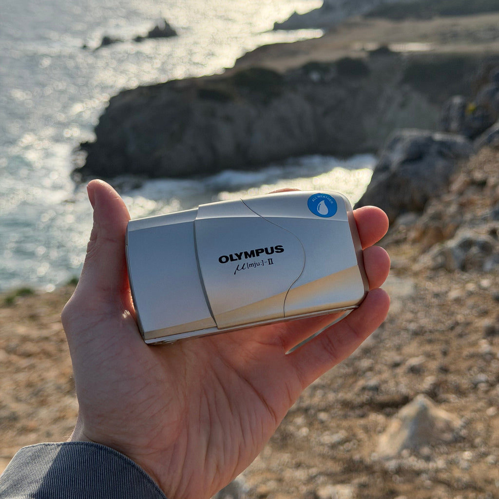 Hand holding an Olympus digital camera with cliffs in the background